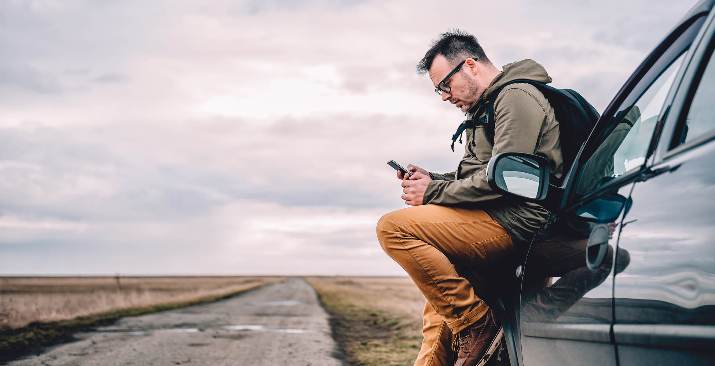 Man sitting on a car looking at phone