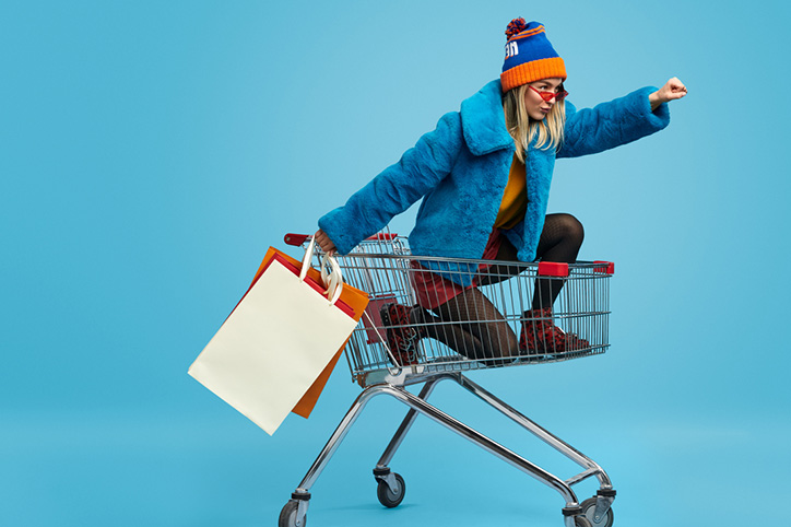 Young lady riding in a shopping cart doing a superman pose