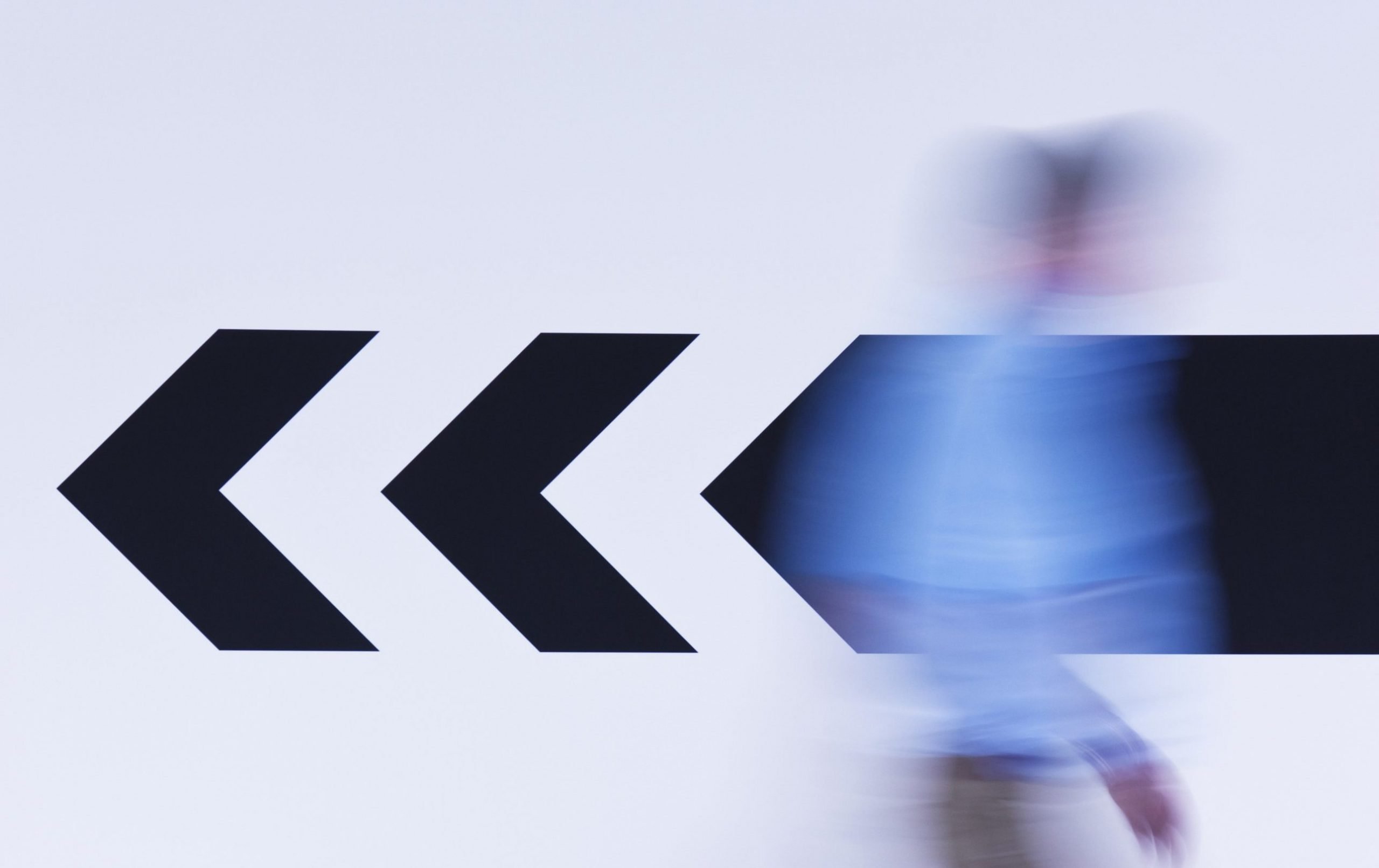 A blurred man walking to the right, while an arrow points left